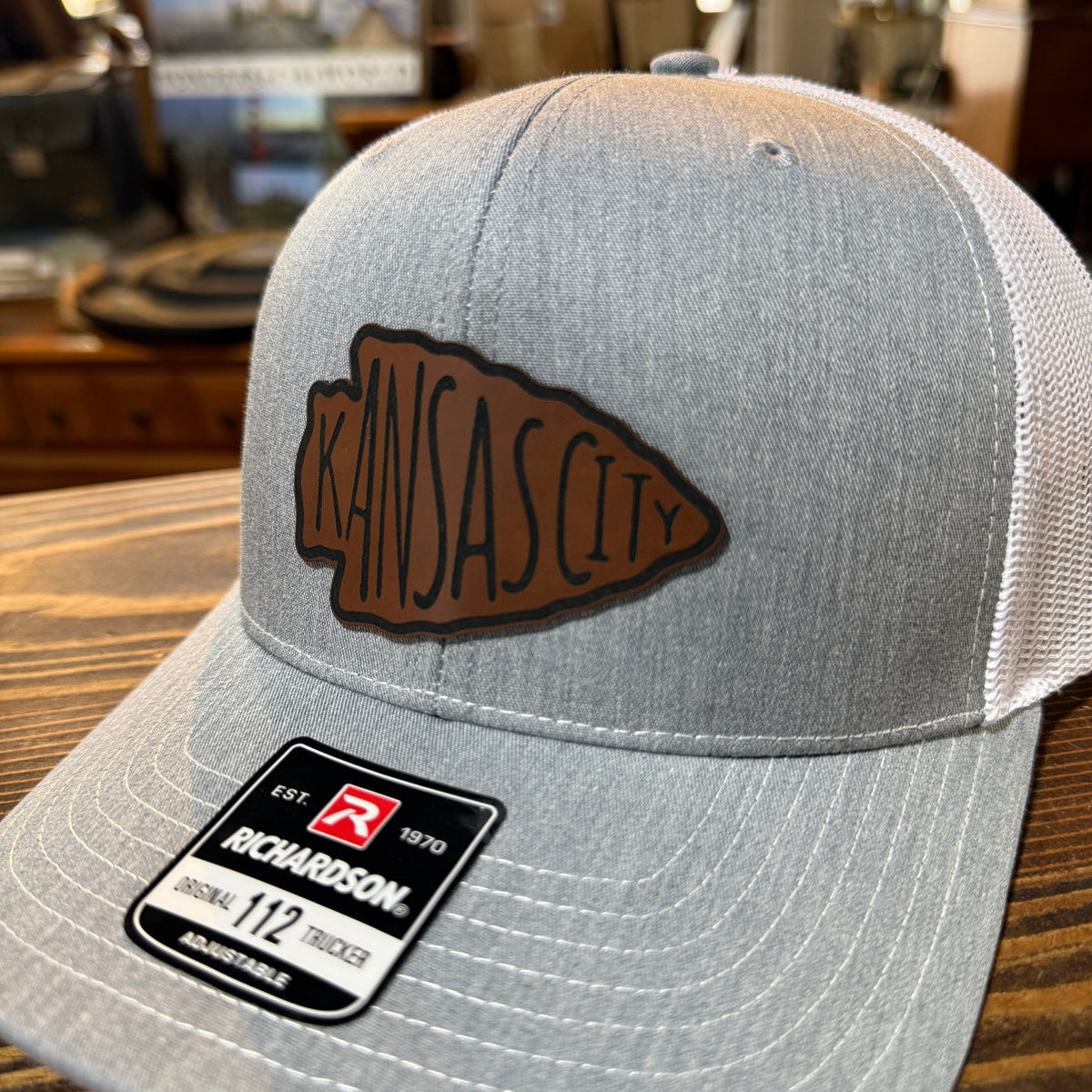 Close-up of brown leatherette Kansas City arrowhead patch on gray Richardson 112 hat