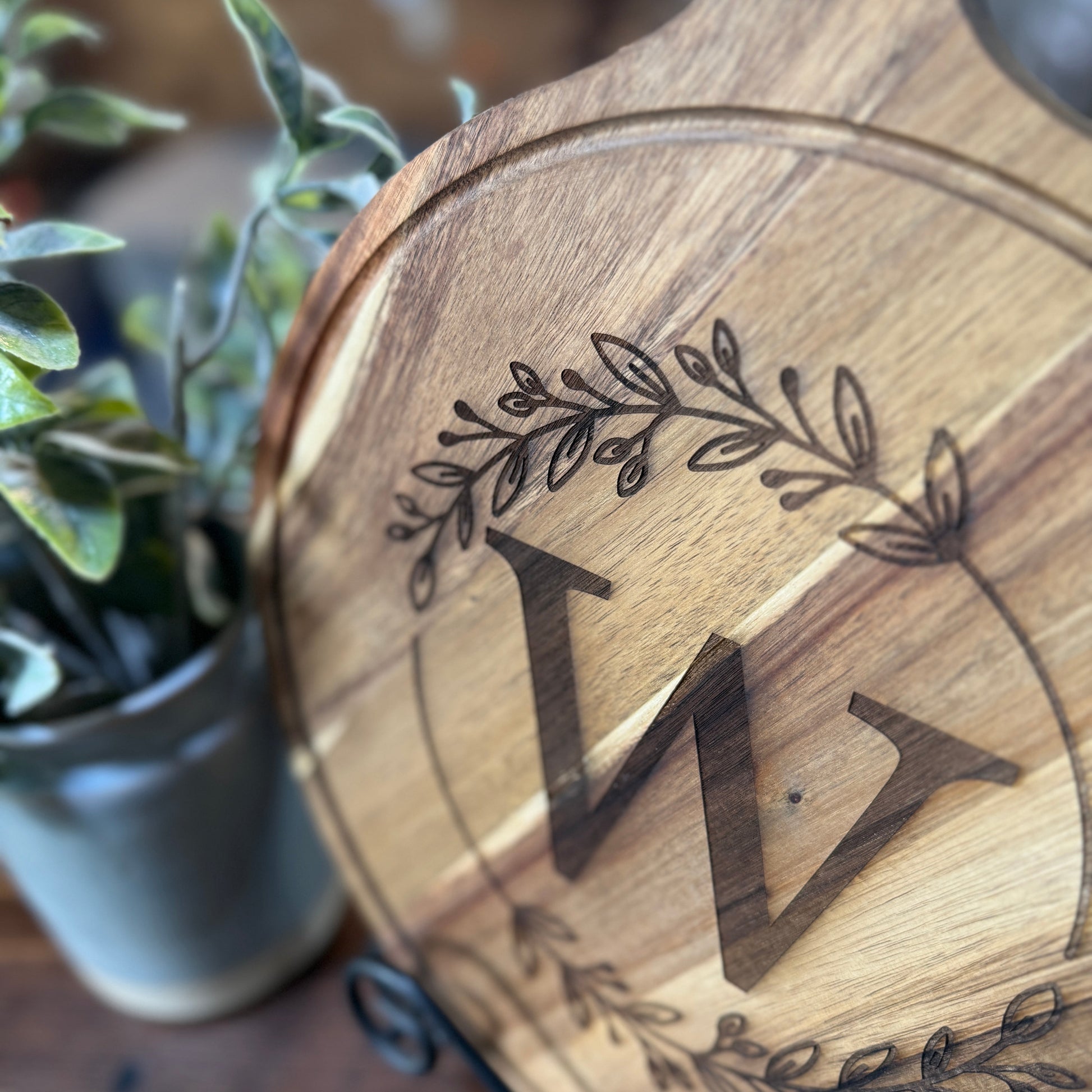 Wooden cutting board with engraved initials and decorative elements on a blurred background